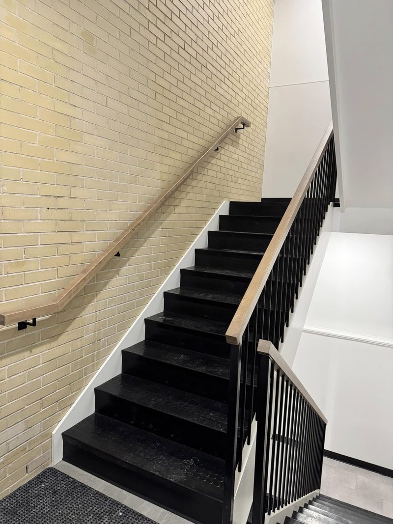 Escalier commercial à marches noires, rampe murale de bois et mur de brique