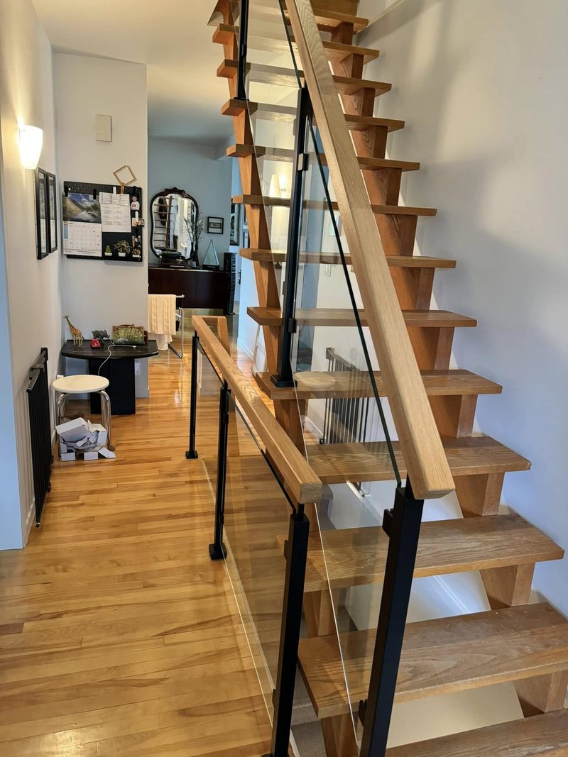 Escalier flottant en chêne longeant un couloir, main courante de bois et poteaux noirs