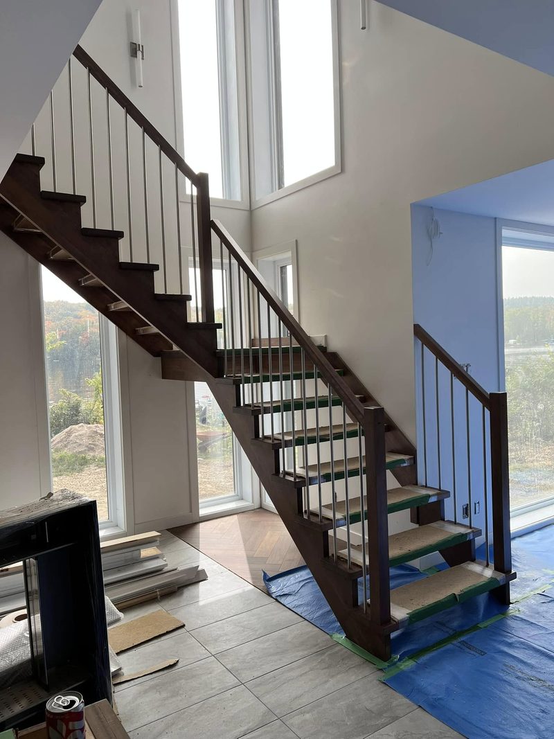 Escalier flottant en bois foncé avec barreaux noirs dans une pièce à haut plafond