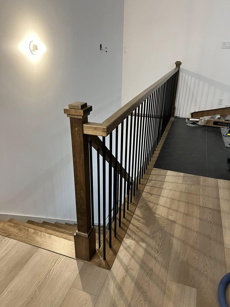 Départ d'escalier avec poteau en bois foncé et barreaux noirs