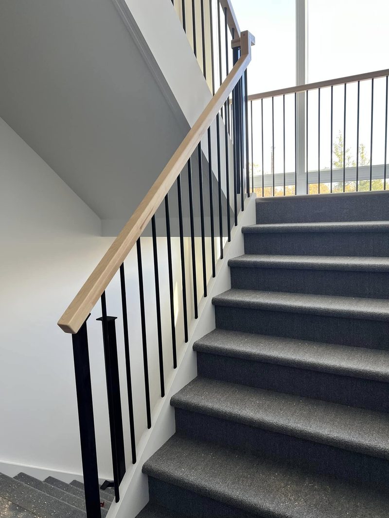 Escalier recouvert de tapis avec main courante de chêne et barreaux noirs