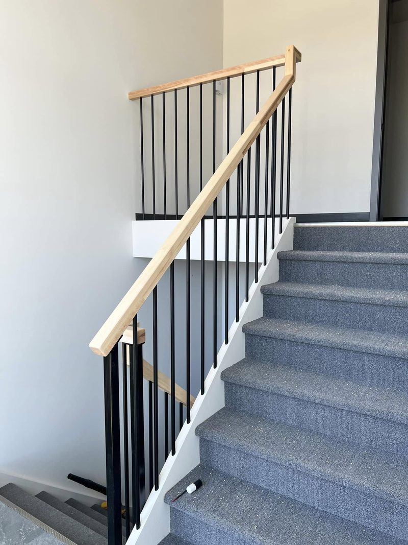 Escalier recouvert de tapis gris, main courante de bois clair et barreaux noirs