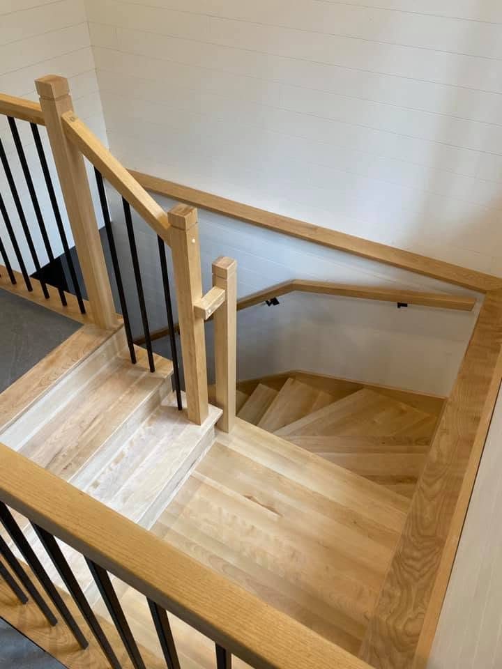 Escalier tournant en bois clair avec poteaux carrés et barreaux noirs, vu de l'étage