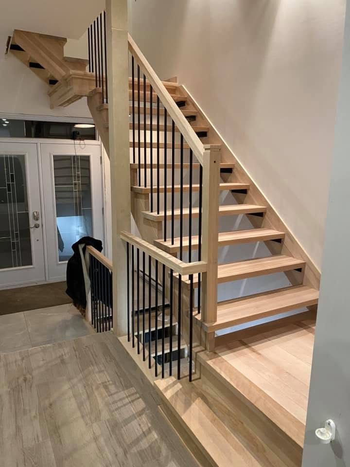 Escalier flottant en bois clair avec barreaux noirs près d'une porte-patio